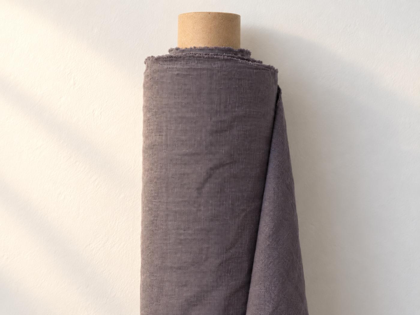 Roll of Purple linen fabric against a white wall in warm side light